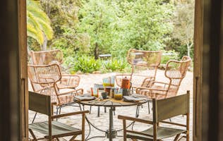 location - Barbarine - Outdoor Terrace with Wicker Furniture  location - Barbarine - Image of an outdoor terrace with wicker chairs and a table, surrounded by lush greenery.