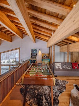 location - ORSO  - Modern game room with wooden decor  location - ORSO  - This modern game room features elegant wooden decor with a foosball table, a comfortable sofa, and a stunning view of the snow.