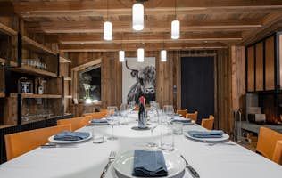 location - ORSO  - Modern dining room with rustic decoration  location - ORSO  - This modern dining room features rustic decoration with wooden elements, orange chairs, and a table elegantly set for a meal. The warm atmosphere is enhanced by a fireplace and a unique wall art piece.