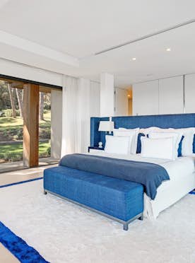 location - Blu - Modern Bedroom with Garden View  location - Blu - Modern bedroom featuring a large bed, blue headboard, and a view of a lush garden through a large window.