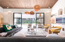 location - Serena - Modern living room with garden view  location - Serena - A modern and elegant living room with a grey sofa, yellow armchairs, and sophisticated interior decor, offering a stunning view of the garden.
