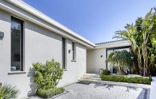 location - Marguerite - Modern house facade with garden  location - Marguerite - Image of a modern house with a white facade and well-maintained garden. The house features modern windows and a cobblestone path leading to the entrance.