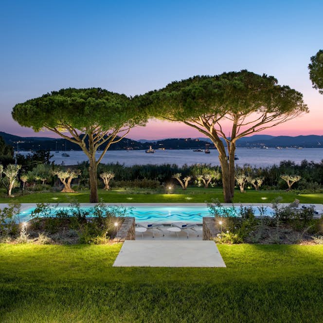 location - Canoubwest - Pool with lake view at sunset  location - Canoubwest - A beautiful outdoor pool with a stunning lake view, surrounded by large trees and well-maintained lawns, illuminated by soft lights at sunset.