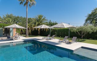 location - Beausoleil - Pool with lounge chairs and umbrellas in a tropical garden  location - Beausoleil - Image of an outdoor pool surrounded by lounge chairs and umbrellas in a tropical garden with palm trees and lush greenery.