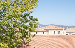 location - Riviera - Panoramic view of rooftops and mountains  location - Riviera - Image of a house with a red-tiled roof, surrounded by mountains and clear blue sky.