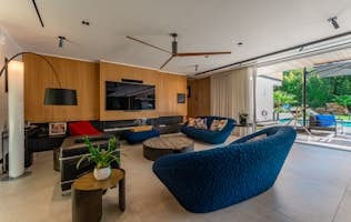 location - Jeanne - Modern living room with pool view  location - Jeanne - A modern living room with blue sofas and a view of an outdoor pool. The space is well-lit with designer lighting and elegant interior decor.