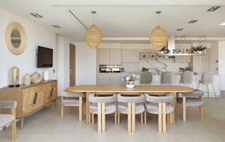 location - Haroma - Modern dining room and open kitchen  location - Haroma - This image shows a modern dining room with a wooden table and grey chairs, as well as an open kitchen with white cabinets and high-end appliances.